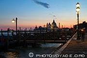 Vue sur le quai près de la place San Marco où se situe l'embarcadère des gondoles avec l'église 
Notre Dame de la Salute à l'arrière plan. La photo a été 
prise après le coucher du soleil, quand l'éclairage public s'allume.