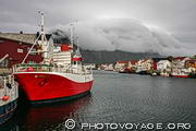 Le petit port de Henningsvaer au sud de l'&icirc;le Austvagoya, 
a &eacute;t&eacute; construit sur un groupe d'&icirc;les au pied d'une falaise dominant la mer. Sur la photo, elle est recouverte  d'un manteau de  nuages.