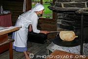 Animation au musée folklorique d'Oslo. Femme en tablier blanc préparant une crêpe cuite sur feu de bois dans une maison norvégienne traditionnelle.